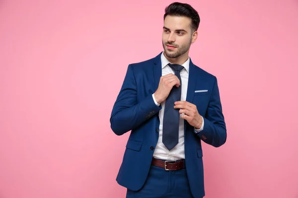 Attractive young man arranging tie on pink background — Stock Photo, Image