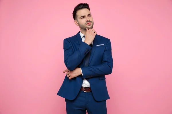 Handsome young man thinking and presenting to side on pink backg — Stock Photo, Image