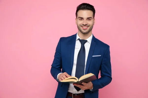 Привлекательный молодой человек держит книгу на розовом фоне в — стоковое фото