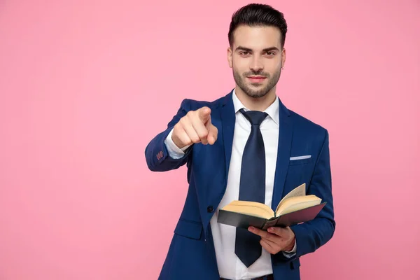 Atractivo joven apuntando con el dedo y sosteniendo libro — Foto de Stock