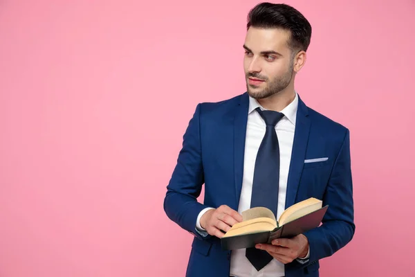 Joven guapo sosteniendo un libro sobre fondo rosa — Foto de Stock