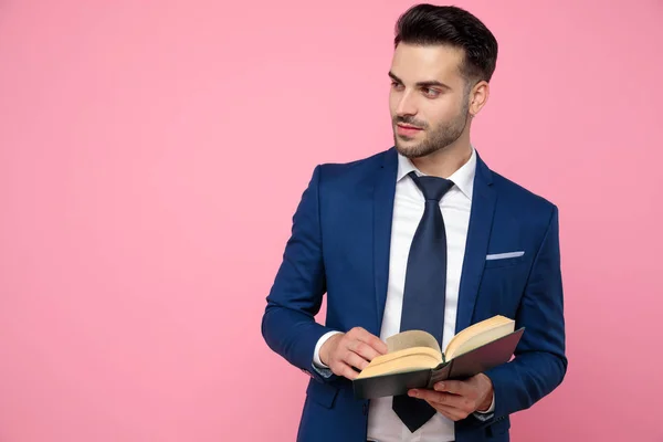 Jovem bonito segurando um livro sobre fundo rosa — Fotografia de Stock