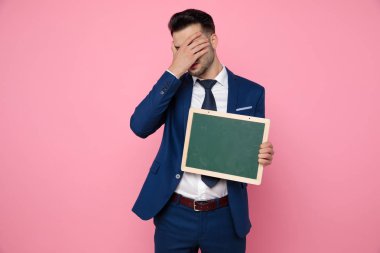 pembe arka plan üzerinde boş bir tahta tutan çekici genç adam