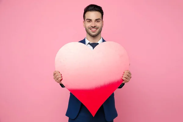 Bell'uomo che tiene un cuore su sfondo rosa in studio — Foto Stock