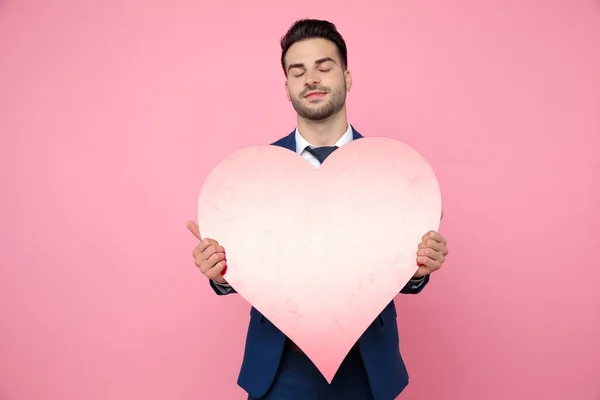 Atractivo joven sosteniendo el corazón sobre fondo rosa — Foto de Stock