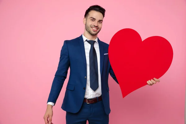 Attractive young man holding a heart on pink background — Stock Photo, Image
