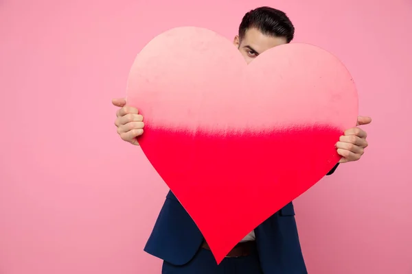 Attraente giovane uomo in possesso di un grande cuore su sfondo rosa — Foto Stock