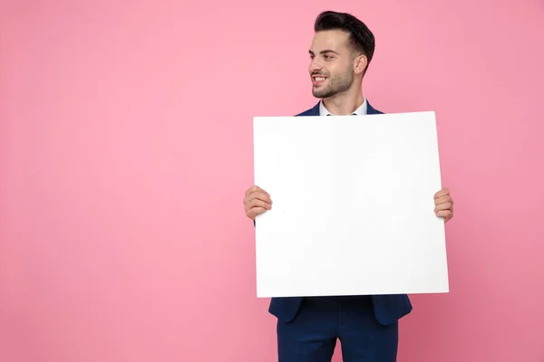 Attraktiv ung man som håller tom bräda på rosa bakgrund — Stockfoto