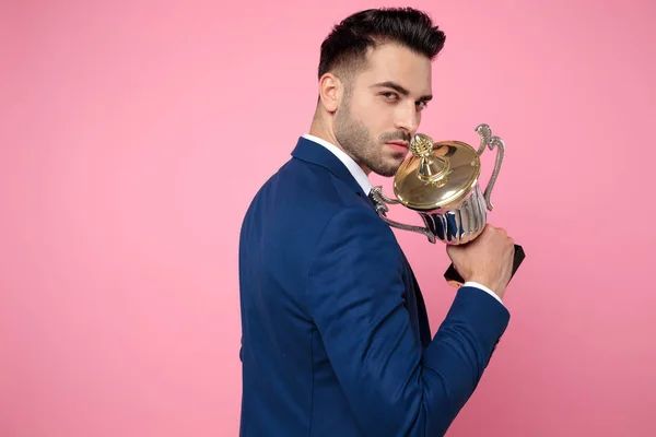 Atractivo joven sosteniendo la copa de la victoria sobre fondo rosa — Foto de Stock