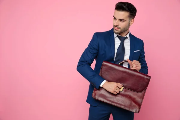 Elegantní příležitostný muž držící kufřík na růžovém pozadí ve studiu — Stock fotografie