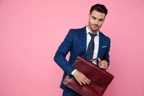 Bellissimo giovane uomo che tiene la valigia su sfondo rosa — Foto Stock