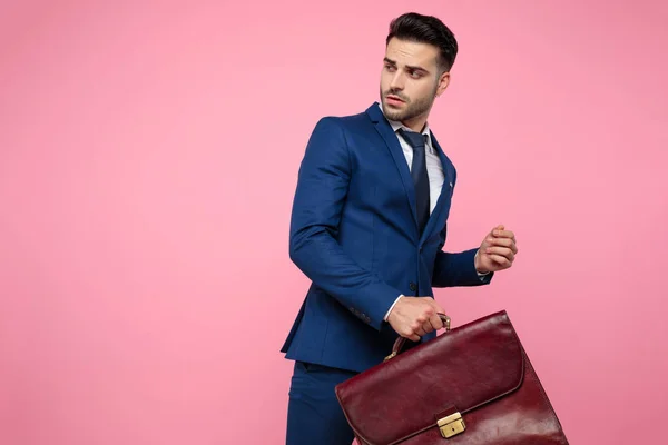 Aantrekkelijke jonge man met een koffer op roze achtergrond — Stockfoto