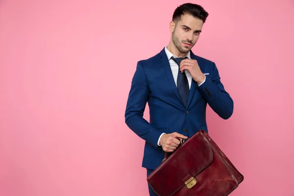 smart casual man fixing tie and holding suitcase