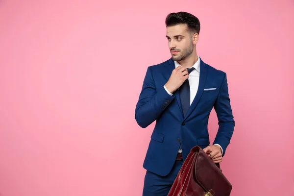 Уверенный молодой человек чинит галстук и держит чемодан — стоковое фото