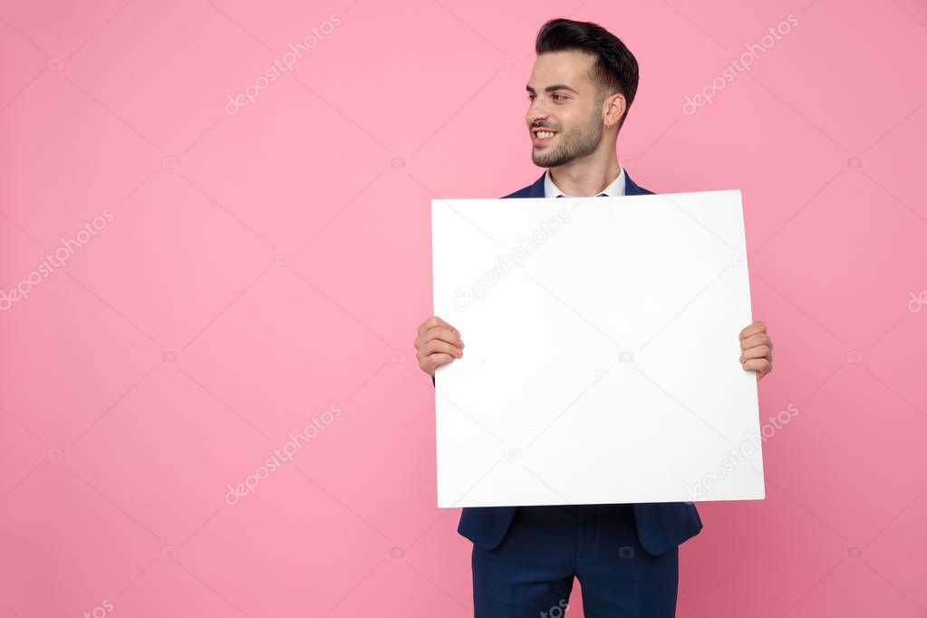 attractive young man holding empty board on pink background