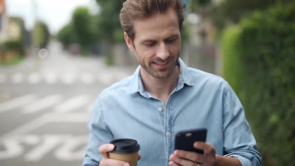 Jovem Homem Casual Caminha Bebe Xícara Café Enquanto Notícias Celular — Vídeo de Stock