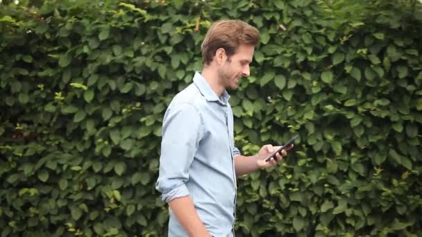 一个快乐的休闲男子走 并在街上的手机发短信的侧视图 — 图库视频影像