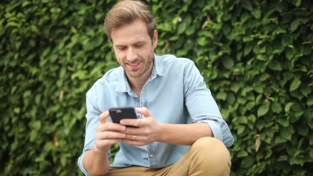 微笑的休闲男子读他的手机和指点相机 — 图库视频影像