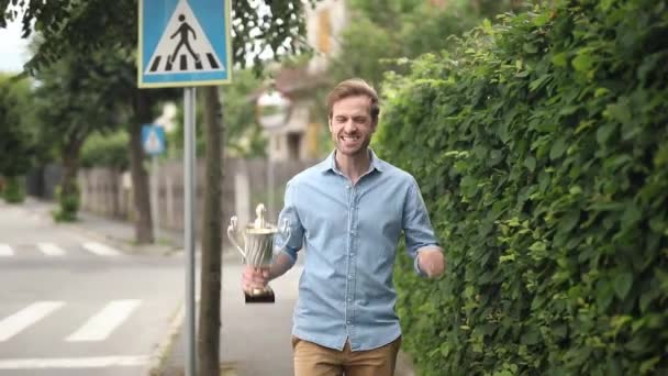 快乐的休闲男子跳的喜悦与他的大奖杯在街上 — 图库视频影像