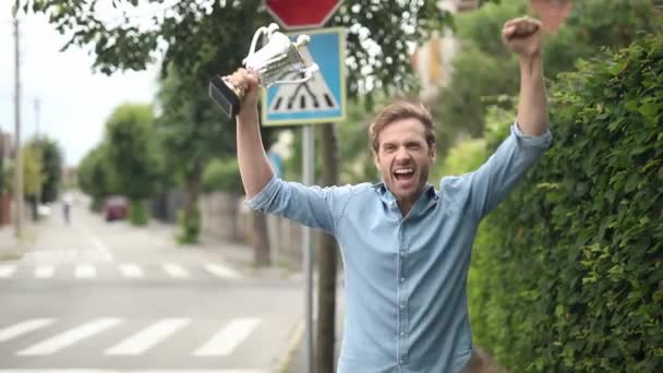 若いカジュアルな男は 大きなトロイのカップを保持し 悲鳴と歓声を持つことによって成功を祝う — ストック動画