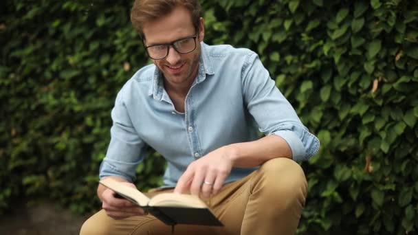 Giovane Casual Indossare Gli Occhiali Sta Leggendo Libro Sulle Ginocchia — Video Stock