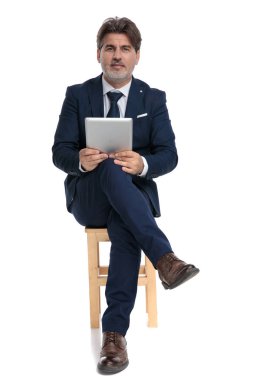 elinde tabletle oturan işadamı kameraya mutlu bakıyor