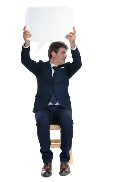 Formal businessman sitting with a speech bubble overhead looking — Stock Photo, Image