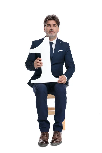 Homem de negócios formal sentado com o número um nas mãos confiante — Fotografia de Stock