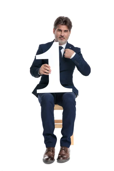Uomo d'affari seduto con il numero uno in mano che indica se stesso — Foto Stock