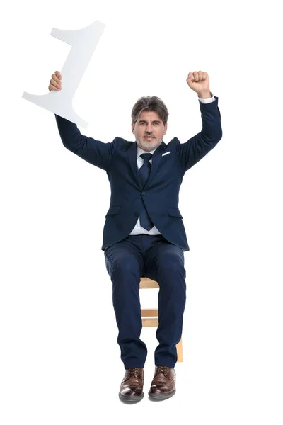 Hombre de negocios formal sentado con las manos en alto y sosteniendo el número uno —  Fotos de Stock
