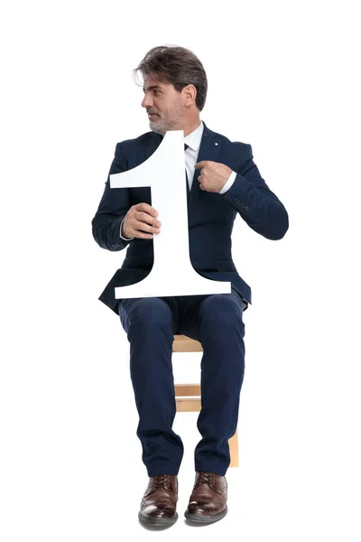 Zakenman zittend met nummer één wijzend naar zichzelf op zoek — Stockfoto