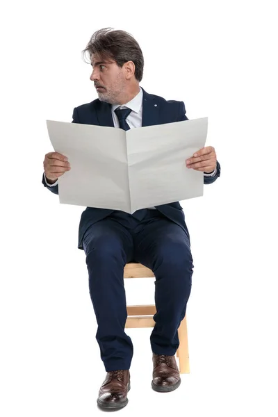 Geschäftsmann sitzt und hält eine Zeitung in der Hand, während er seitwärts schaut — Stockfoto