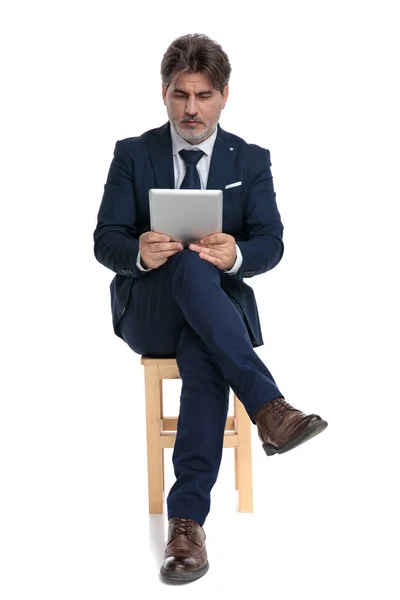 Hombre de negocios sentado y mirando su tableta comprometida — Foto de Stock