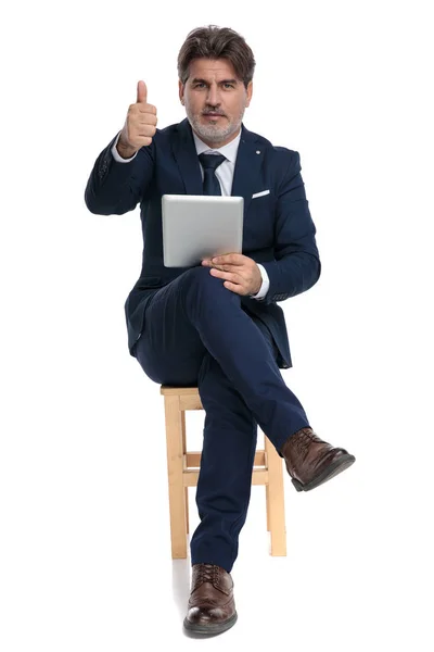 Empresário sentado e segurando um tablet com sinal ok confiante — Fotografia de Stock