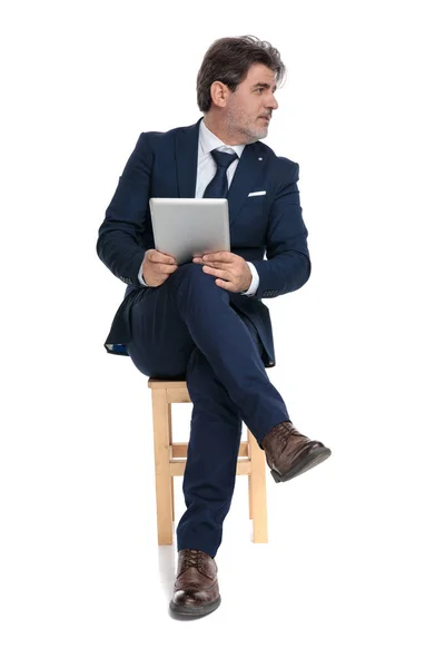 Business man sitting and holding his tablet while looking sideway — стоковое фото