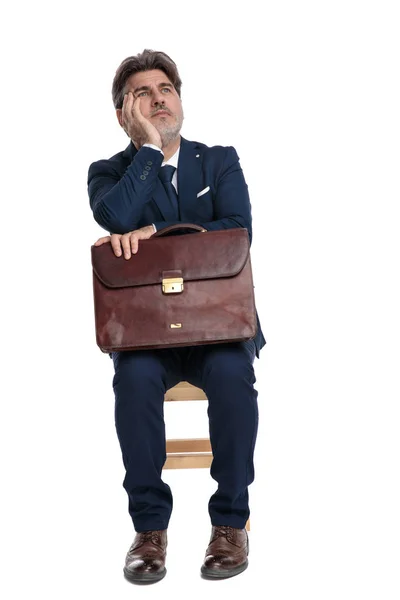 Homem de negócios sentado com pasta em voltas olhando para cima pensativo — Fotografia de Stock