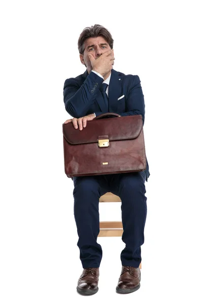 Geschäftsmann sitzt mit Aktentasche auf Schoß und hält Hand über Fac — Stockfoto
