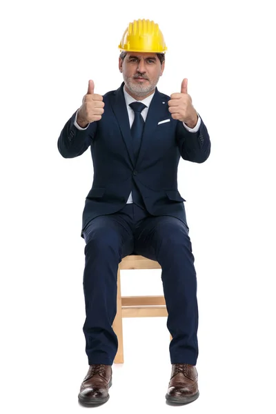 Geschäftsmann sitzt mit Schutzhelm und doppeltem Okay-Schild — Stockfoto