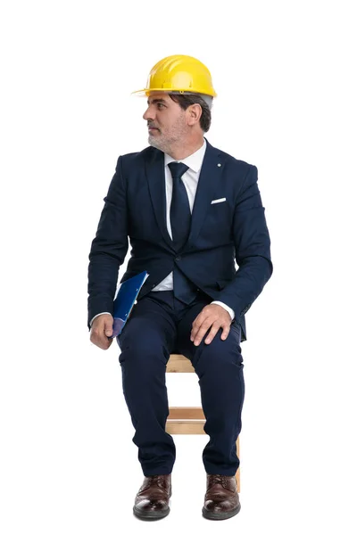 Businessman with safety helmet and clipboard looking sideways — Stock Photo, Image