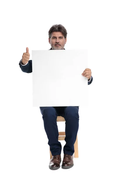 商人坐在一个广告牌，做一个确定的标志 — 图库照片