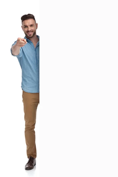 Lässiger Mann, der hinter Plakatwand steht und nach vorne zeigt — Stockfoto