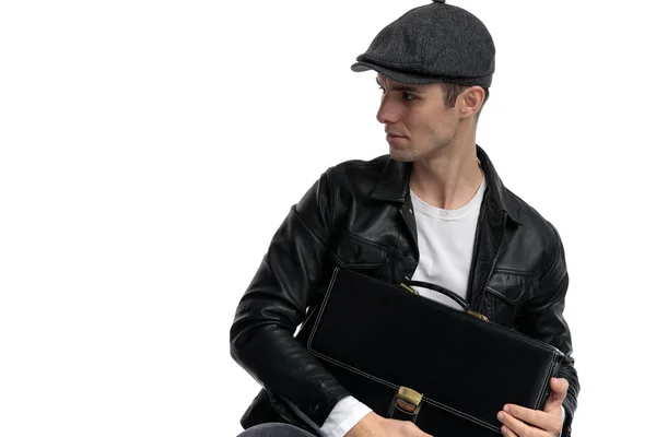 Seated casual man holding briefcase and looking sideways curious — Stock Photo, Image