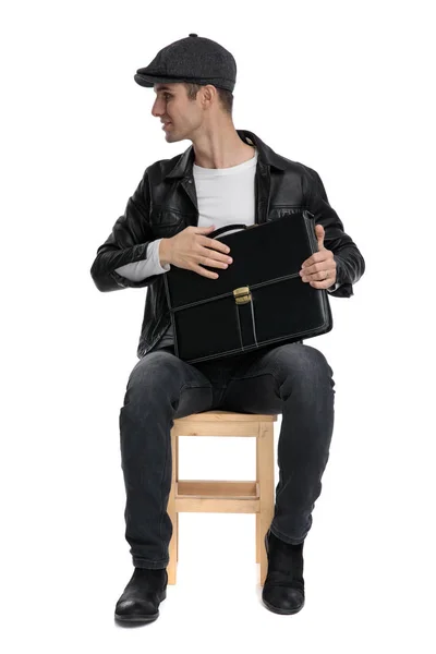 Sentado hombre casual sosteniendo un maletín y mirando hacia los lados feliz —  Fotos de Stock