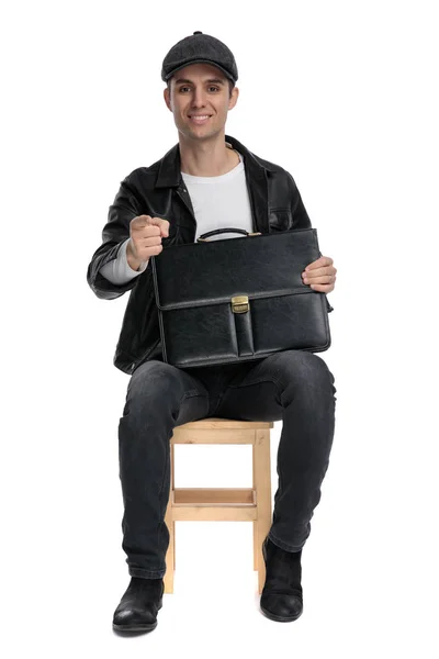 Sentado hombre casual sosteniendo un maletín y apuntando hacia adelante —  Fotos de Stock
