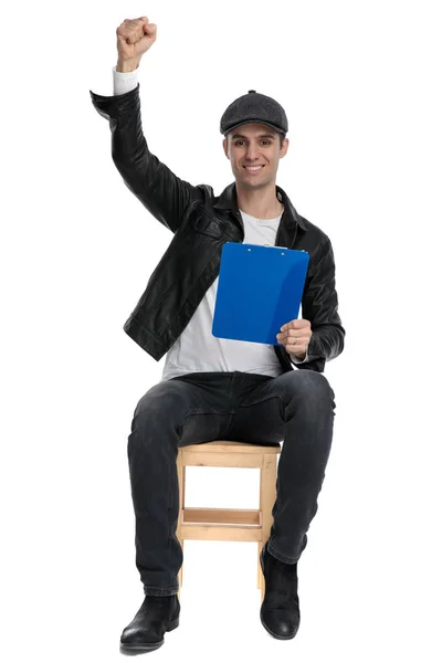 Seated casual man holding clipboard and fist up victorious — Stock Photo, Image