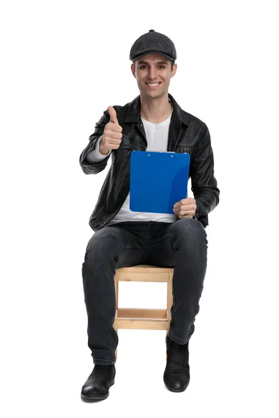 Sentado casual homem segurando prancheta e fazendo ok sinal — Fotografia de Stock