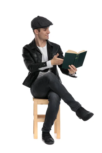 Sitzender lässiger Mann, der sein Buch vorstellt und seitwärts schaut — Stockfoto