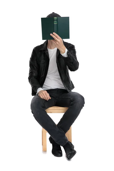 Sitzender lässiger Mann, der sein Gesicht mit einem Buch verhüllt — Stockfoto