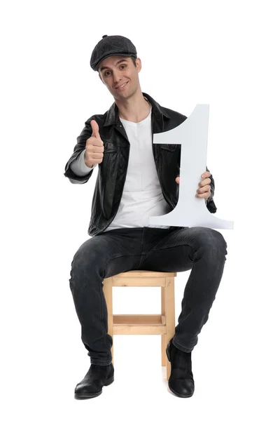 Κάθεται casual άνθρωπος κρατώντας το νούμερο ένα και κάνοντας εντάξει σημάδι — Φωτογραφία Αρχείου