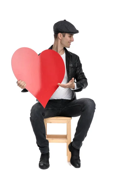 Sentado casual homem apresentando seu grande coração para um lado — Fotografia de Stock